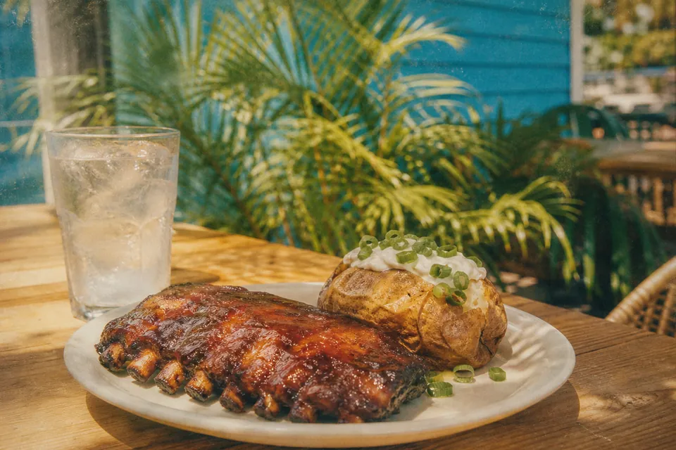 A plate of barbecue ribs with a loaded baked potato